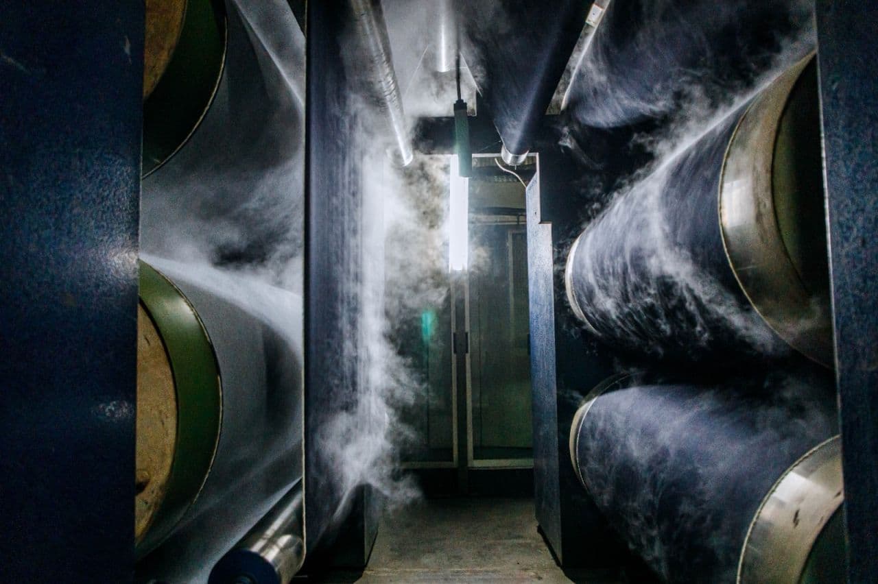Argon Denims finishing floor: indigo denim rolls stacked in trolley carts beside inspection bays.